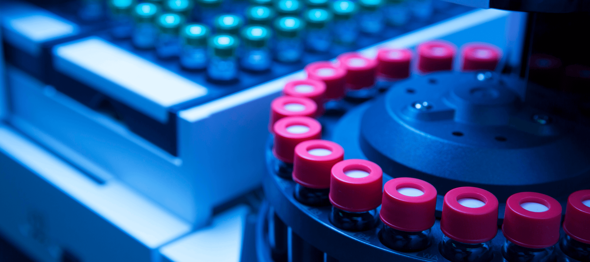 Close-up of automated laboratory equipment processing research vials with red caps, highlighting high-throughput manufacturing and precision handling in a controlled setting.