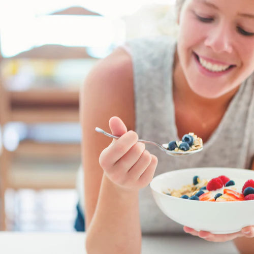 Smiling woman eating a healthy bowl of fruits and oats, representing the transformative benefits of peptides for health and wellness